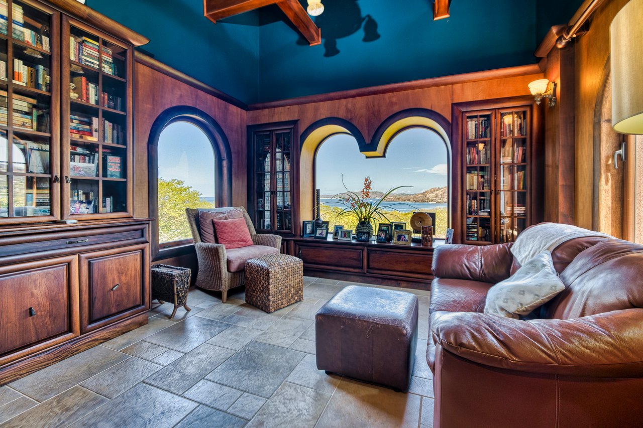 Living room with built-in bookcases, arched windows overlooking the bay, and a leather sofa.