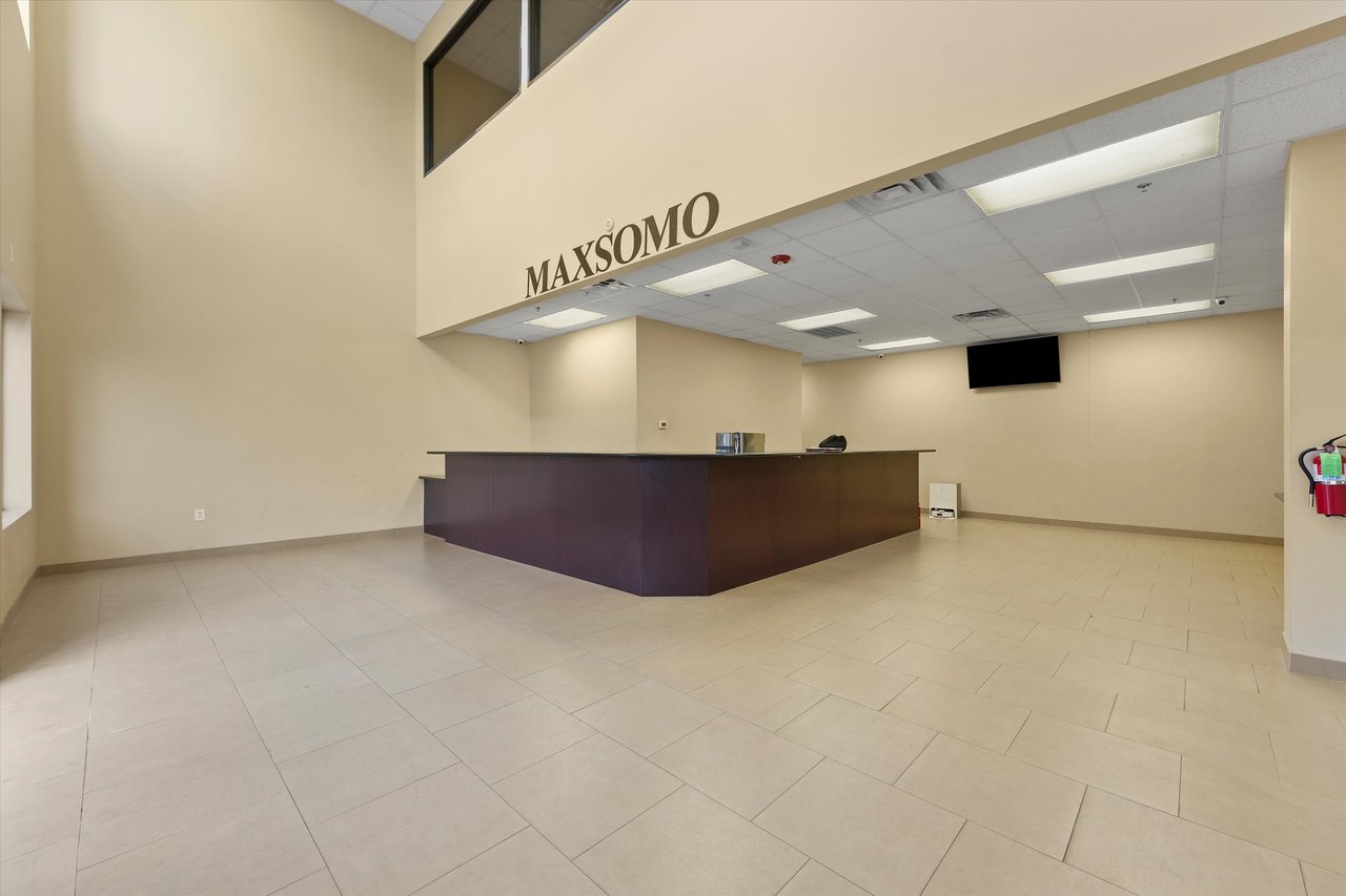 Commercial reception lobby with a dark angular desk, tiled floor, and MAXSOMO wall lettering.