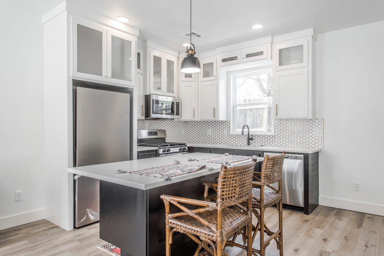 Bright kitchen with white cabinets, stainless steel appliances, hexagonal tile backsplash, and island seating.
