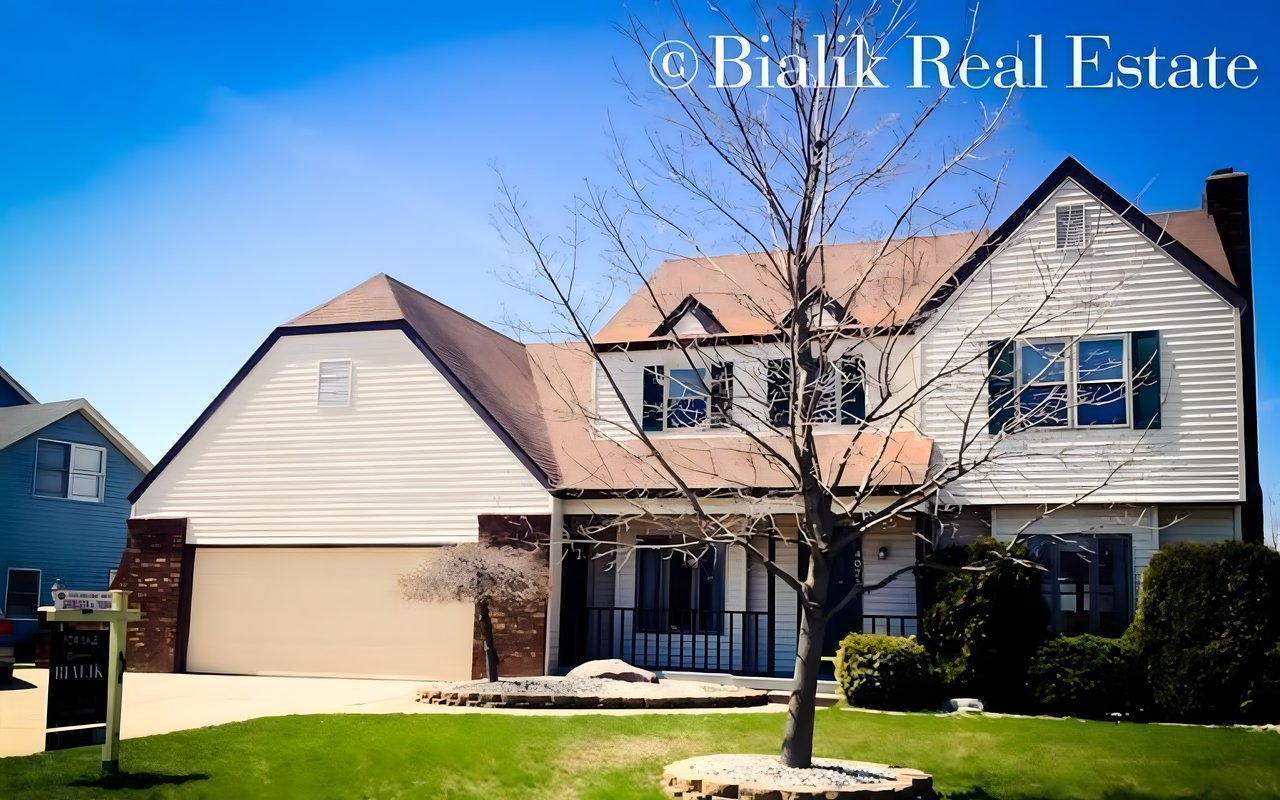 Two-story white-sided house with an attached double garage and leafless tree in the front yard.