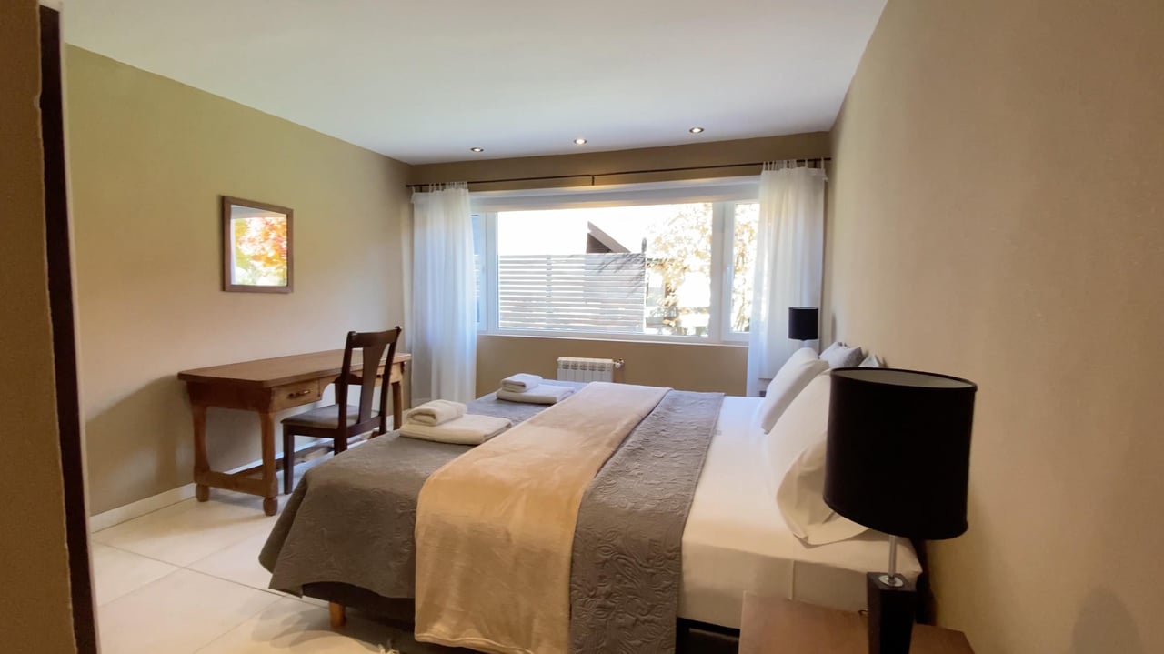 Bedroom with a large bed, wooden desk, and wide curtained window.