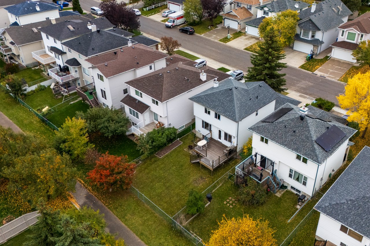 Aerial view of detached homes and fenced backyards with decks and autumn trees.