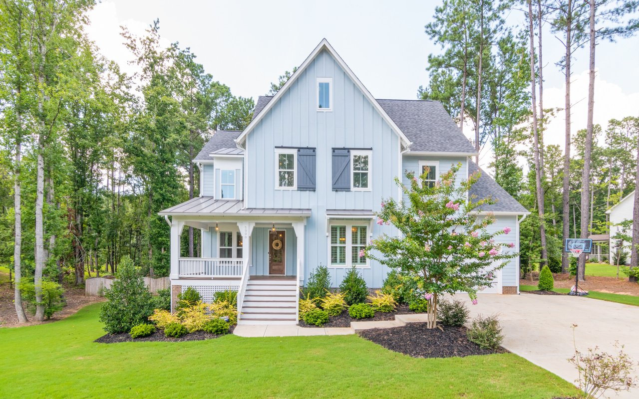 Light blue two-story house with a steep gable, covered porch, and flowering front landscaping.