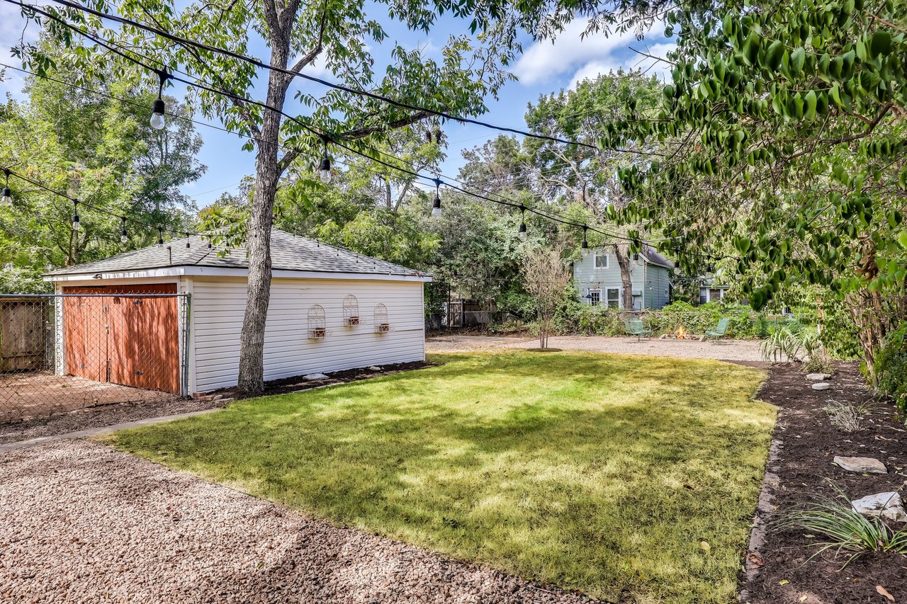 Backyard with a broad lawn, detached shed, overhead string lights, and gravel paving.