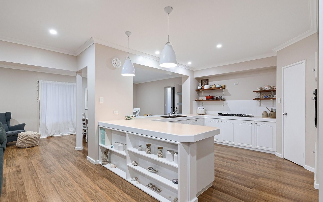 Open-plan kitchen with a large white island, pendant lights, and wood flooring.