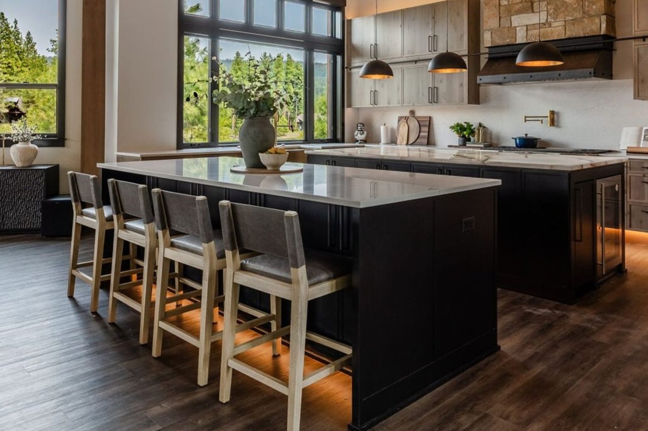 Modern kitchen with a large island, bar seating, and tall windows overlooking greenery.