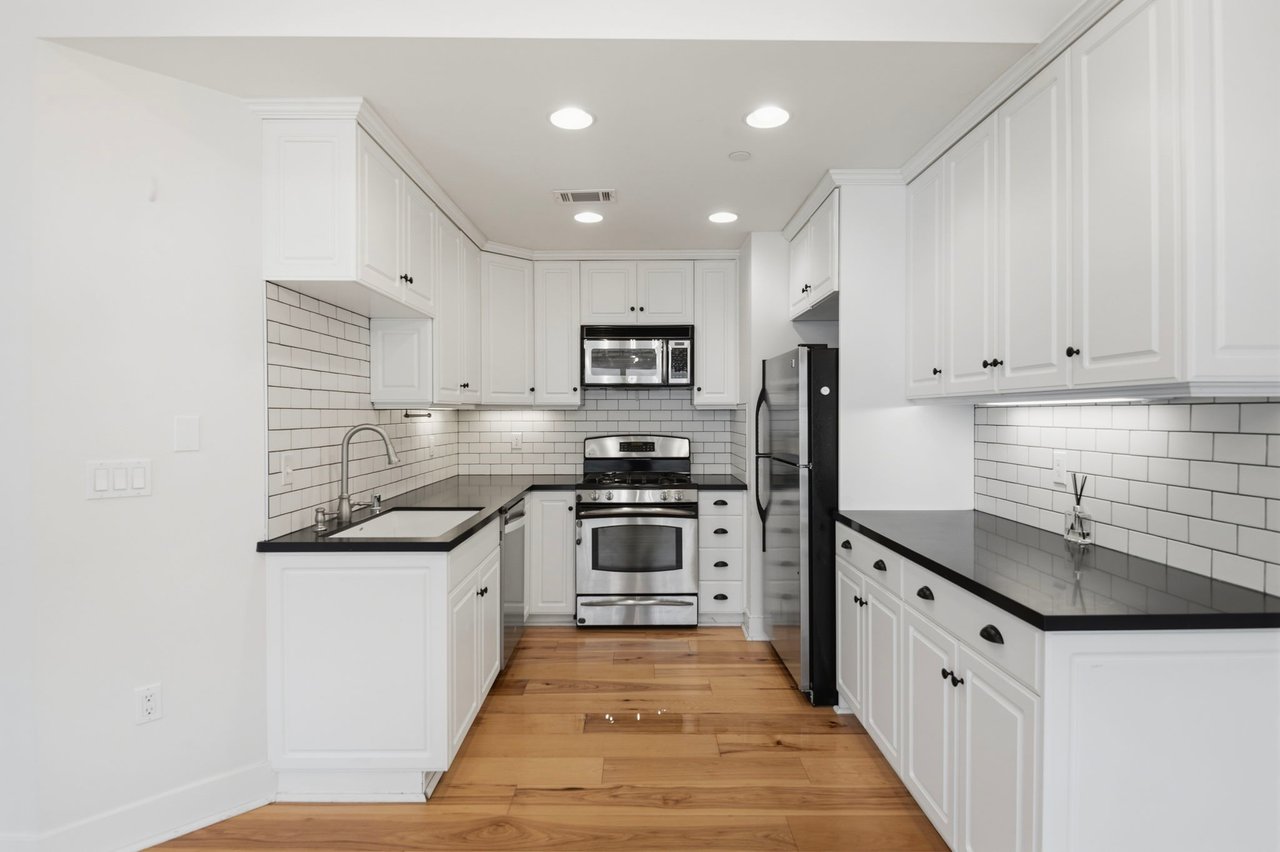 Bright kitchen with white shaker cabinets, dark granite countertops, subway tile backsplash, and stainless steel appliances