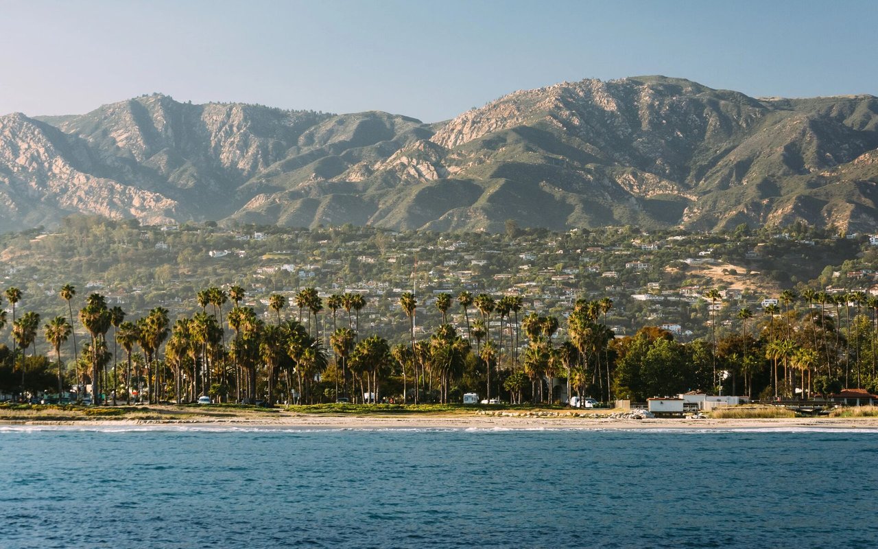 Santa Barbara coastline with a palm-lined shore, city, and mountains.
