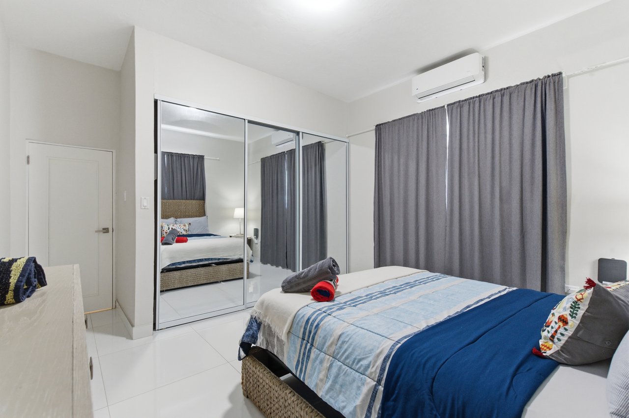 Furnished bedroom with blue bedding, mirrored closet doors, gray curtains, and a wall-mounted air conditioner.