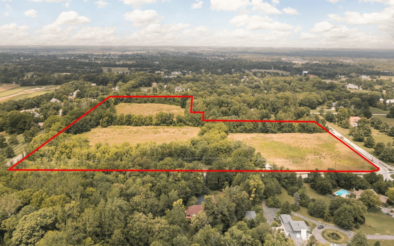 Aerial drone photo showcasing a massive development lot outlined in red, highlighting expansive open acreage, mature wooded borders, and proximity to suburban neighborhoods.