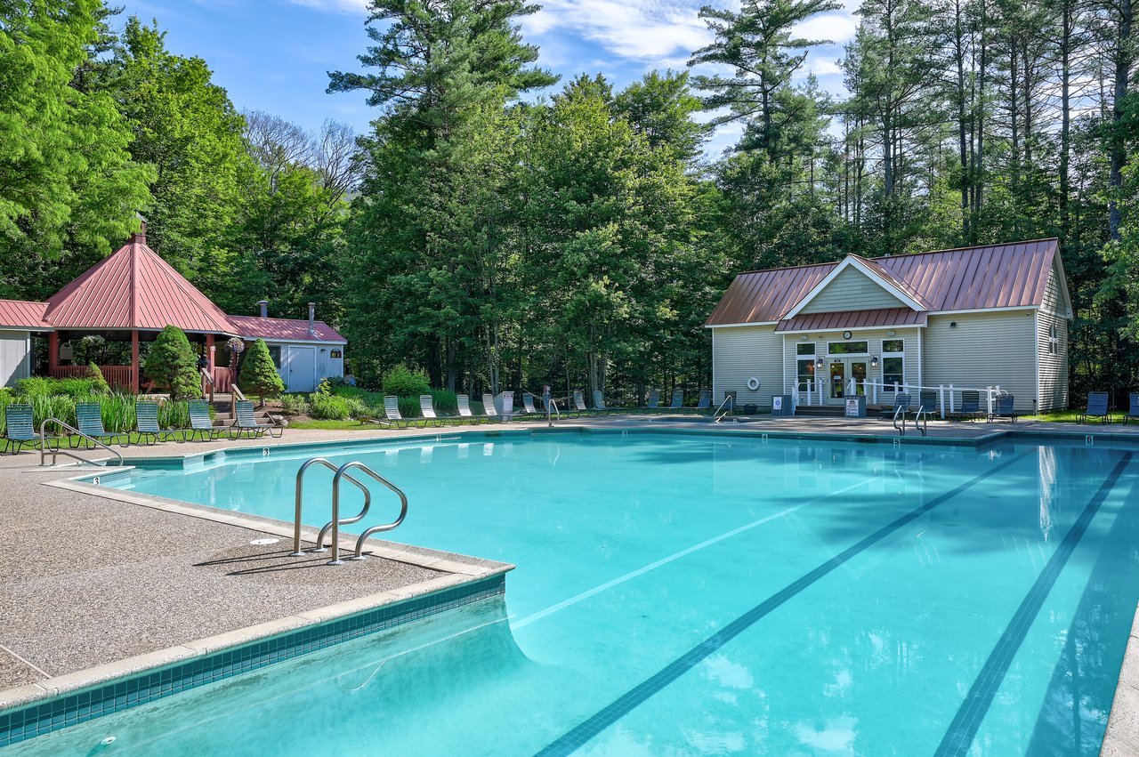 Outdoor pool with a gazebo, clubhouse, and forested surroundings.