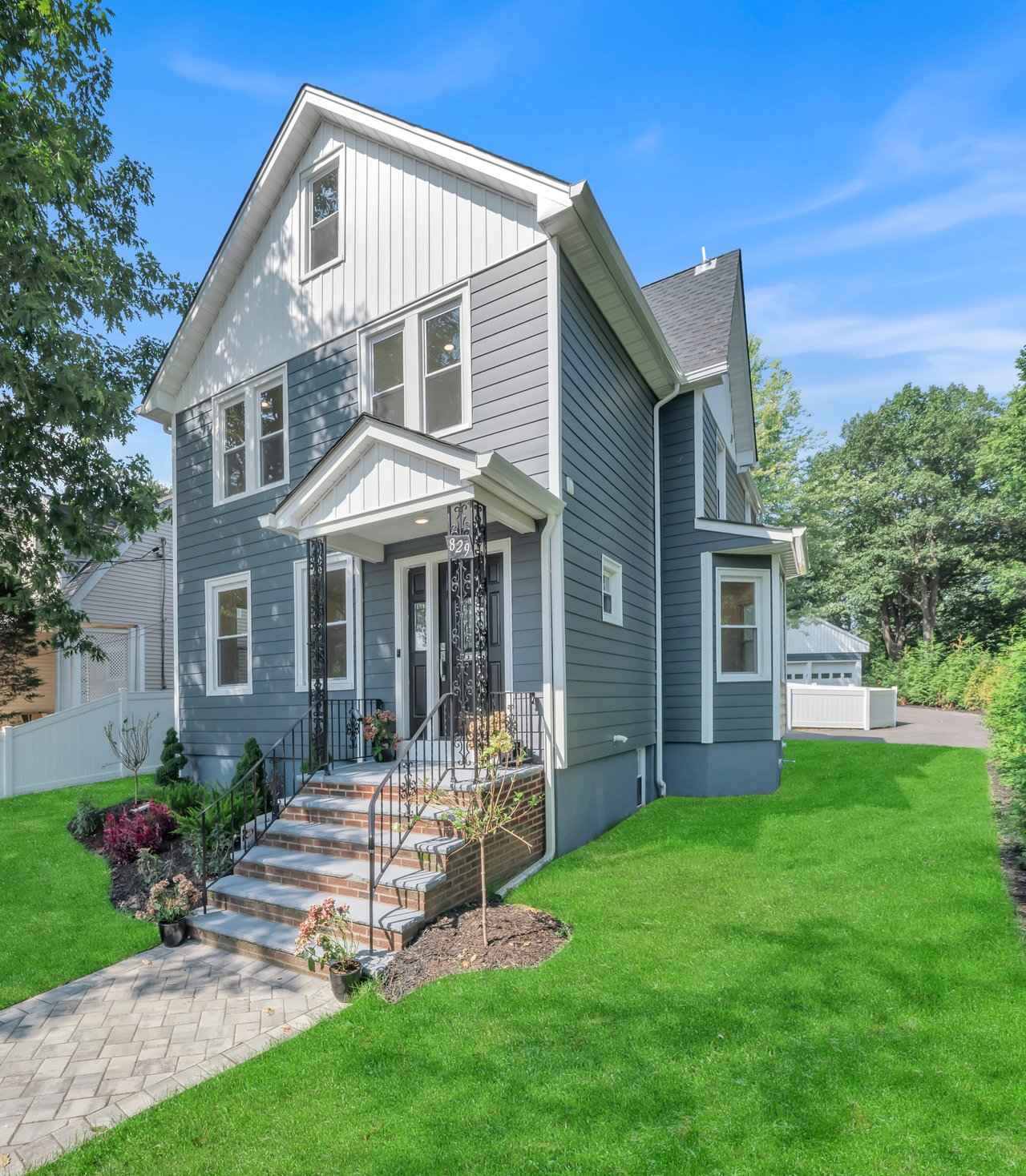 Two-story blue-gray house with white trim, brick steps, and a landscaped front lawn.