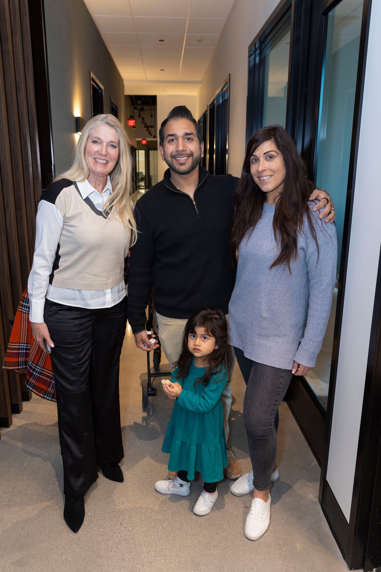 Three adults and a young child pose together in a hallway; the child wears a teal dress.