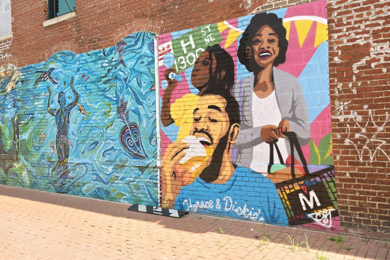 Colorful Bronx street mural with portraits and blue aquatic imagery along a brick sidewalk.