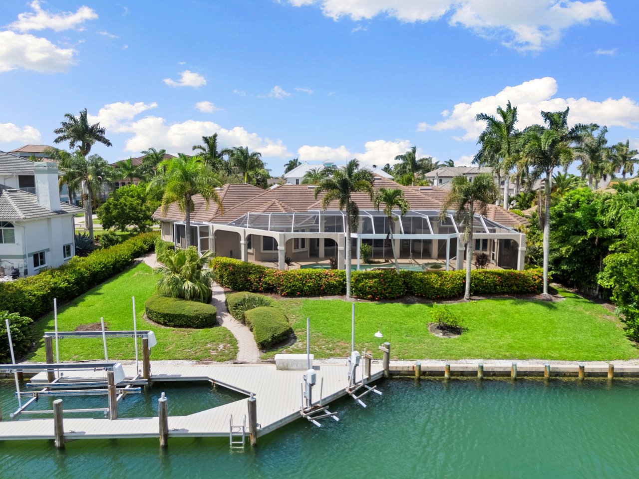 Waterfront home with a screened lanai, palm-lined lawn, and private canal dock.