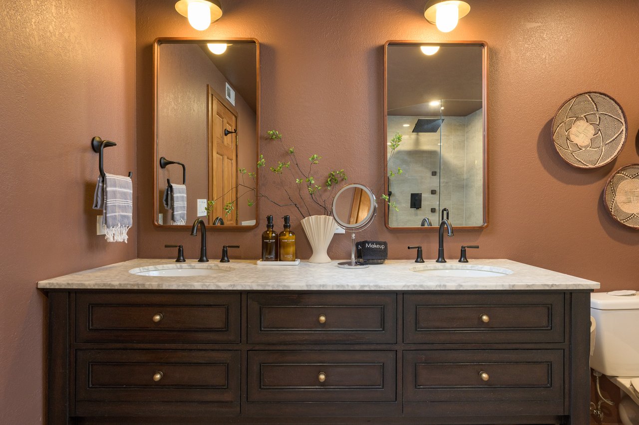 Bathroom with a dark wood double vanity, two framed mirrors, and a glass shower.