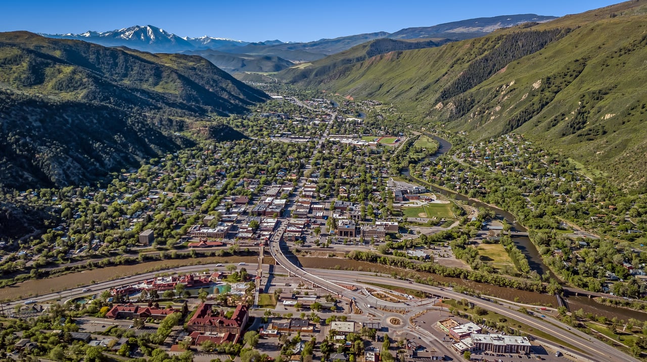 Mountain town in a valley, with a winding river and snow-capped peaks in the distance.