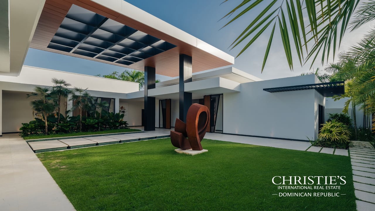 Modern villa with a landscaped courtyard, sculptural canopy, tropical plants, and a lawn sculpture.