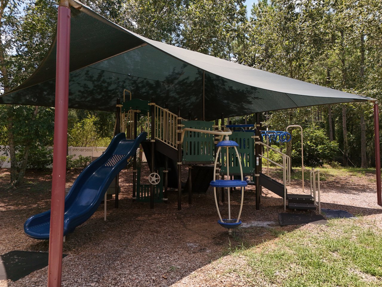 Community playground with blue slides and climbing equipment beneath shade sails.