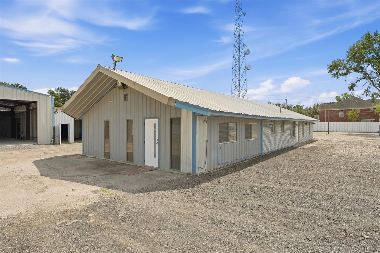 Single-story metal-sided building with blue trim on a gravel lot beside a communications tower.