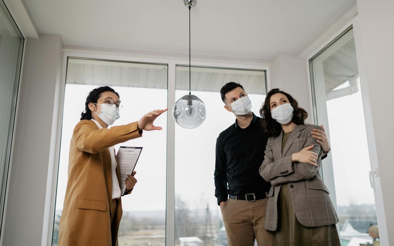 A real estate agent shows a bright, windowed room to a couple during a home viewing.