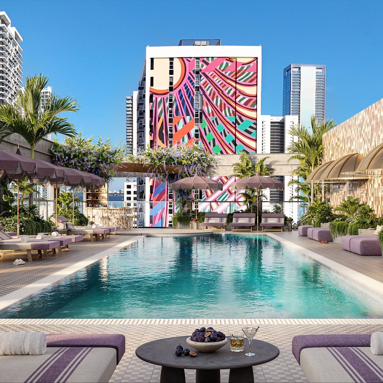 Rooftop pool at The Rider Residences, framed by palm trees, lounge seating, and a colorful mural.