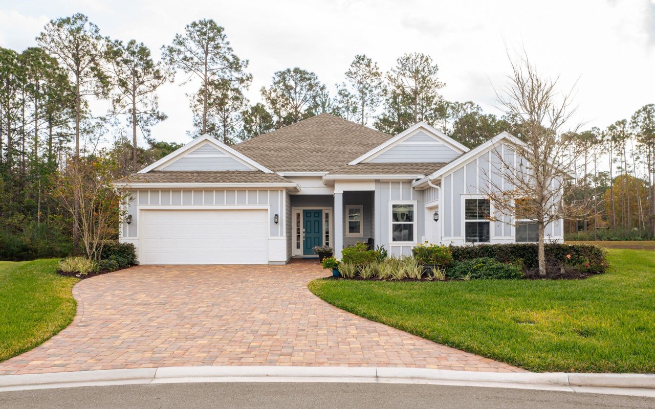 Gray-and-white house with a teal front door, double garage, and curved brick-paver driveway.