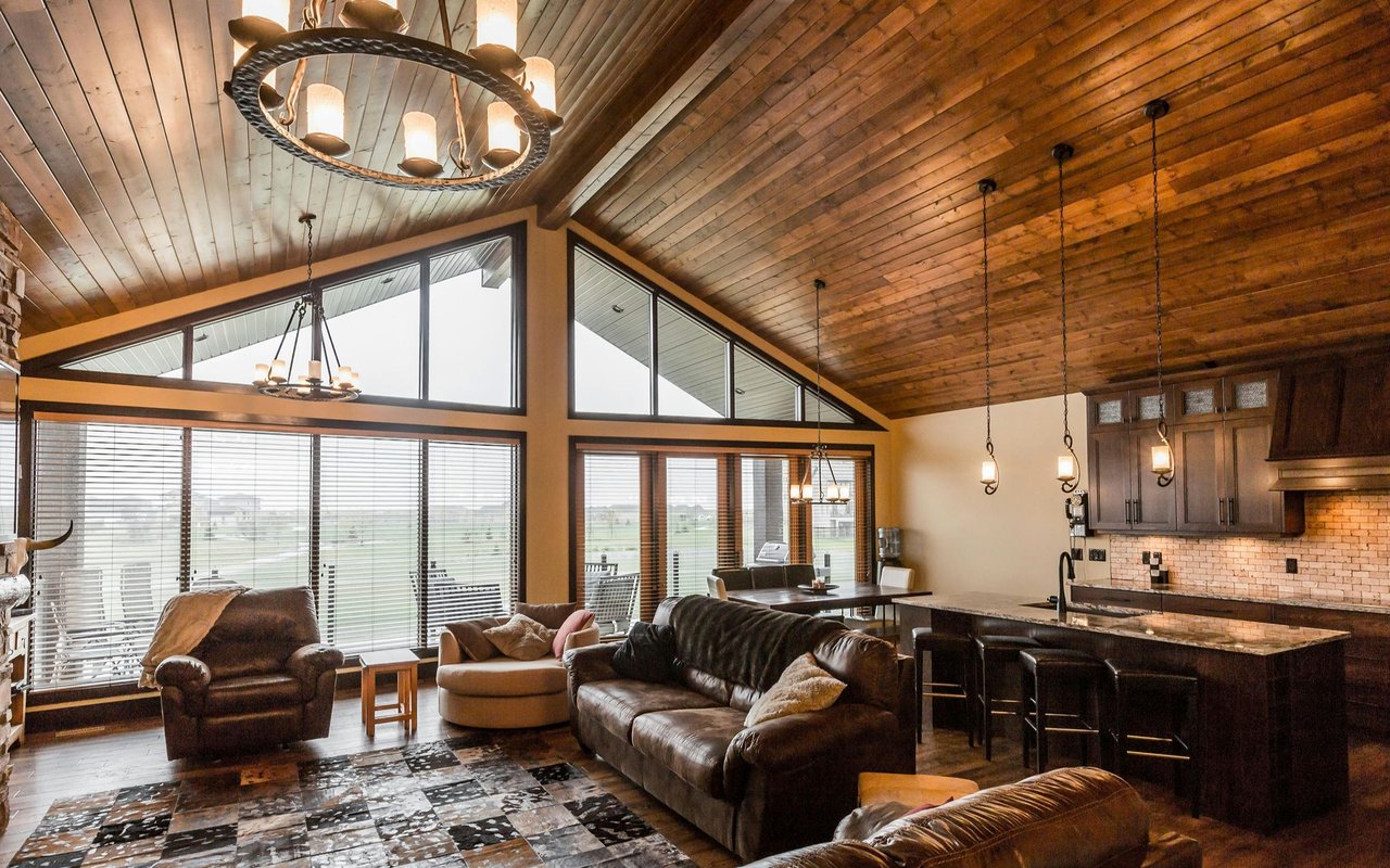 Open living room and kitchen with a vaulted wood ceiling, large windows, and dark leather seating.