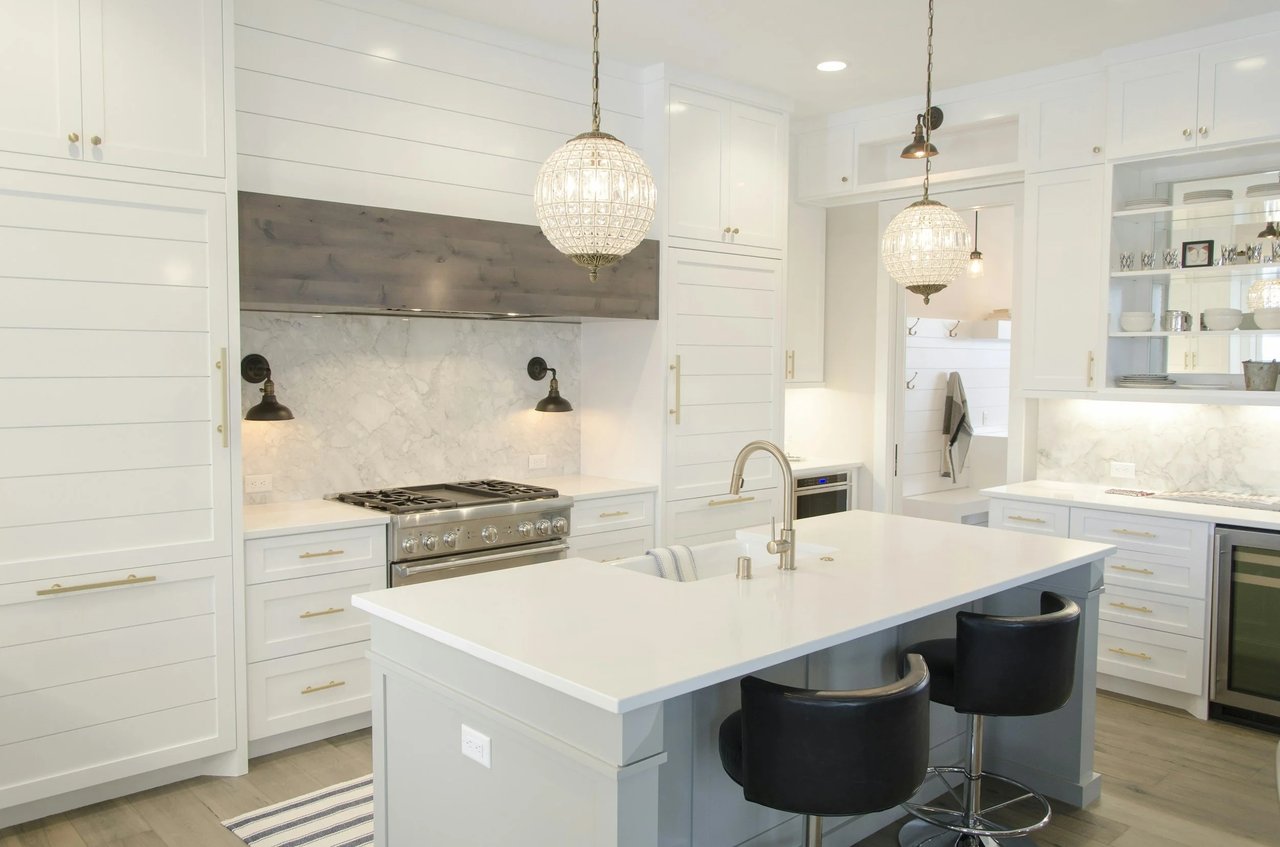 White kitchen with a large island, marble backsplash, and two glass pendant lights.