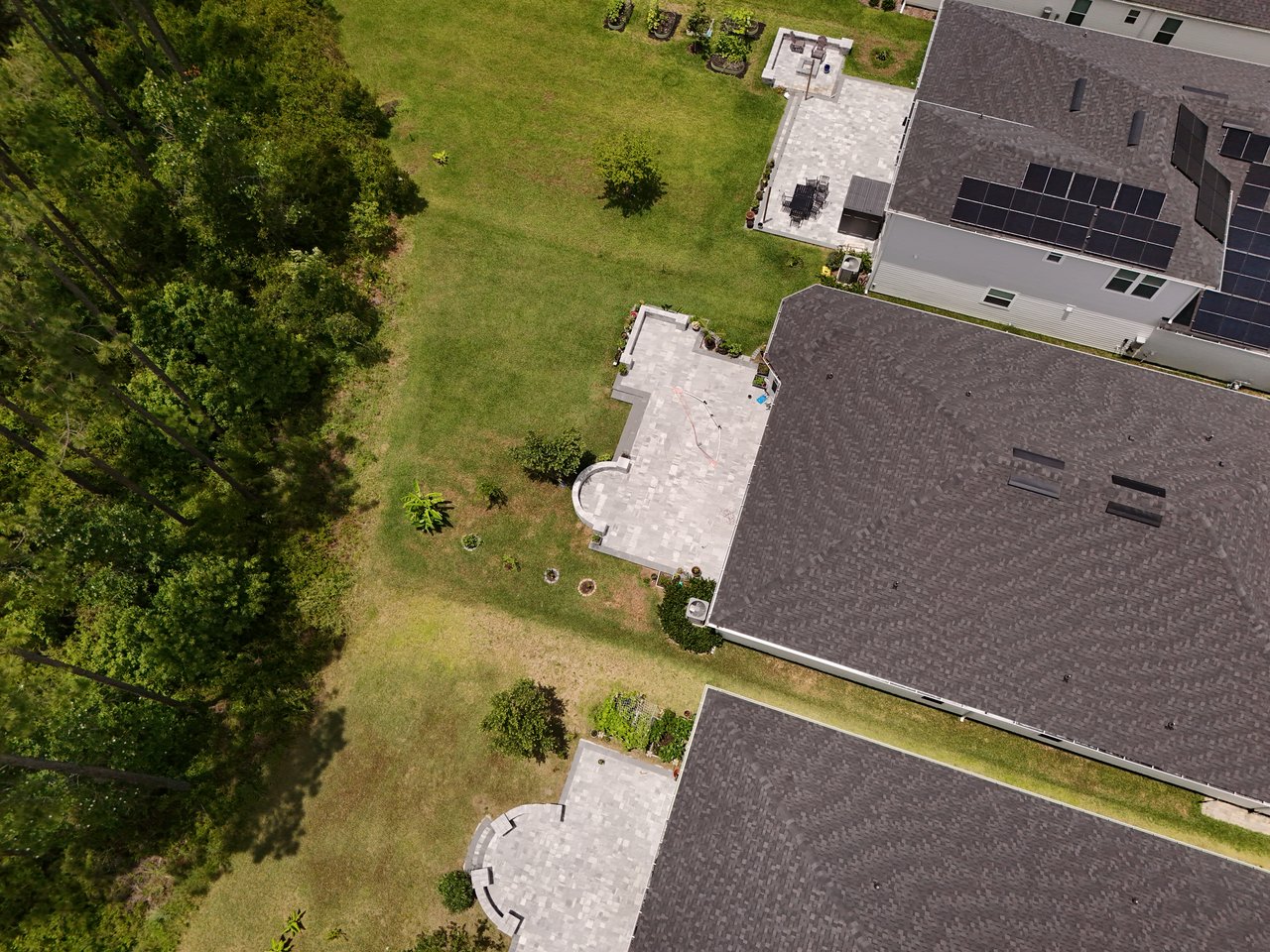 Aerial view of homes with grassy backyards, paved patios, and rooftop solar panels.