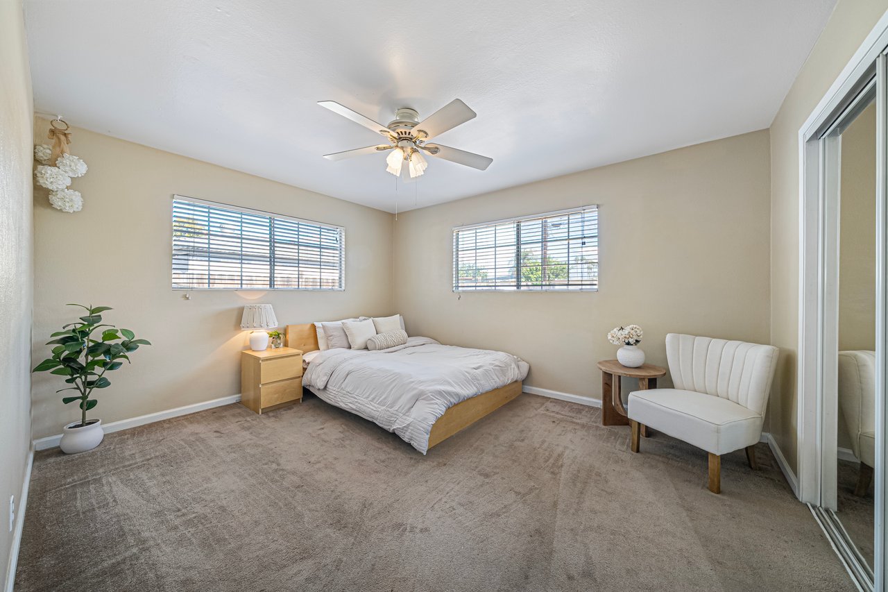 Bedroom with a low bed, beige carpet, ceiling fan, and mirrored closet doors.