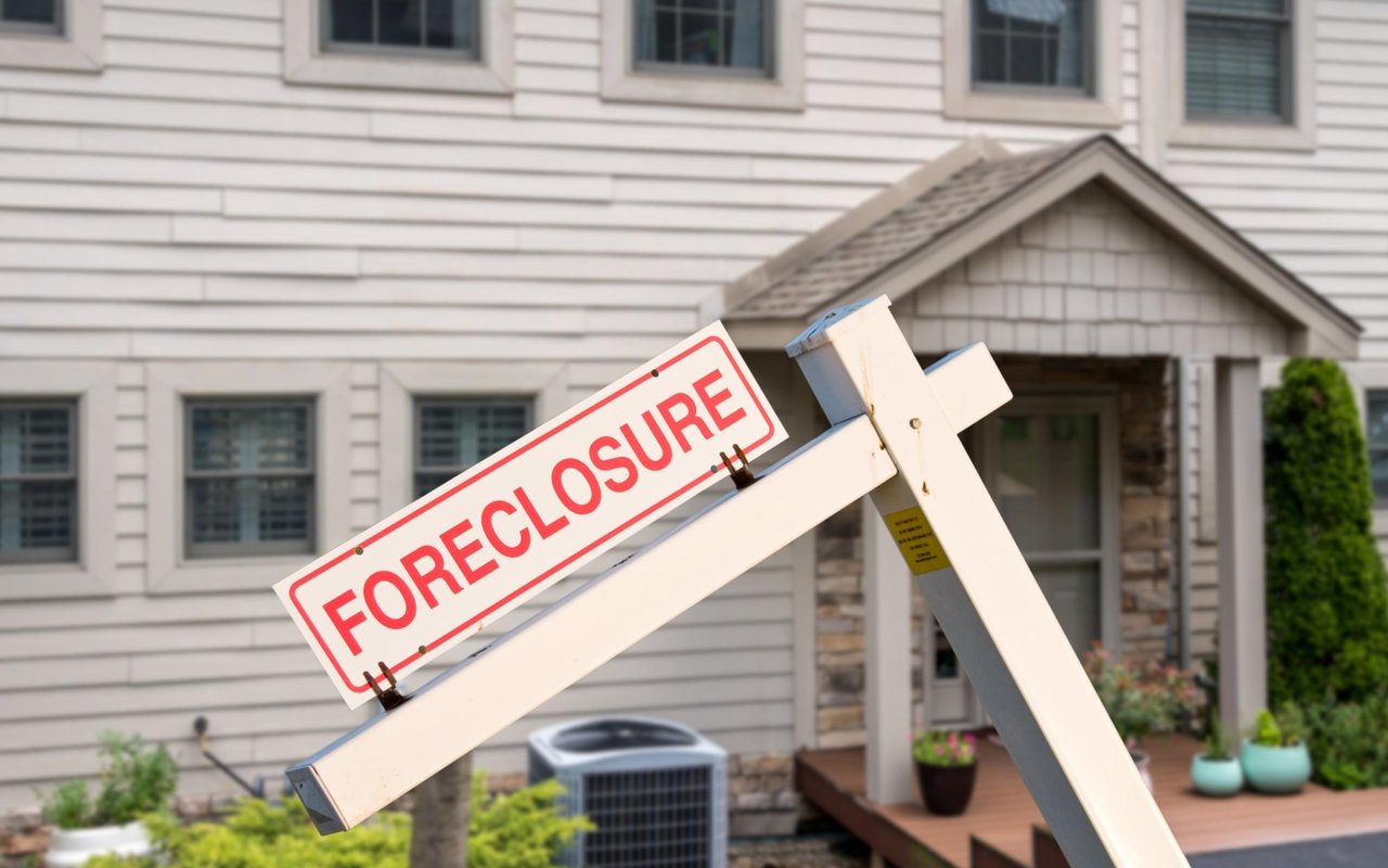 Foreclosure sign mounted on a post in front of a two-story house.