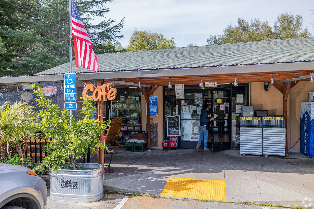 Neighborhood café and market storefront with a covered entrance, American flag, and accessible parking signs.