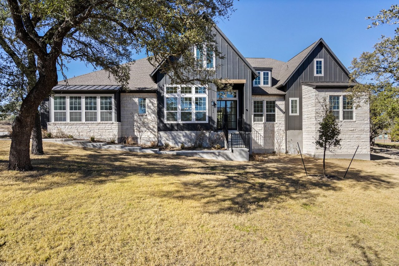 Front elevation of this Ashton Woods contemporary farmhouse home at 133 Mataro Cove in the Cortaro neighborhood of Dripping Springs, Texas, framed by mature oak trees.