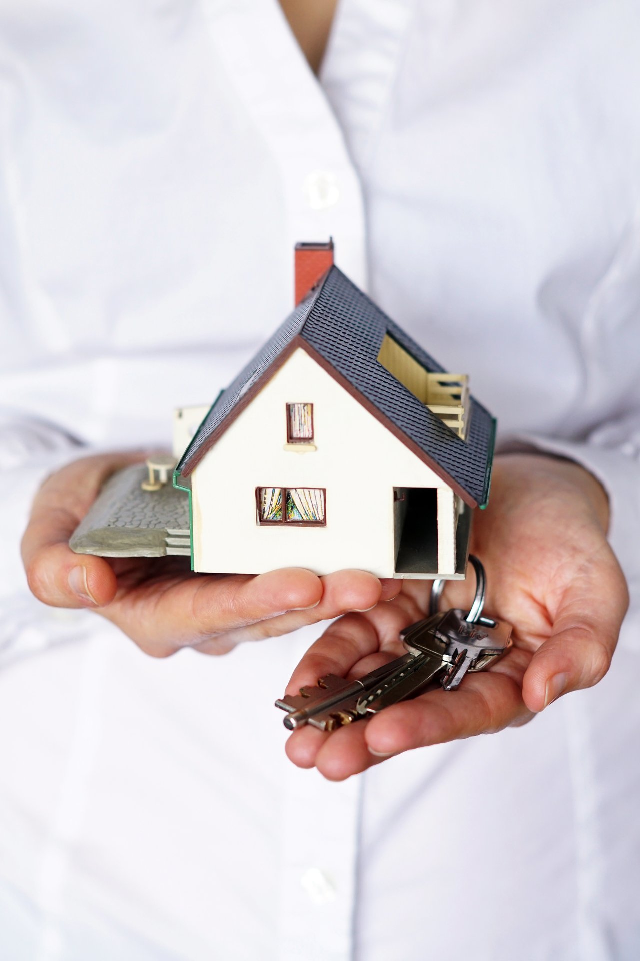 Hands holding a miniature house and keys.