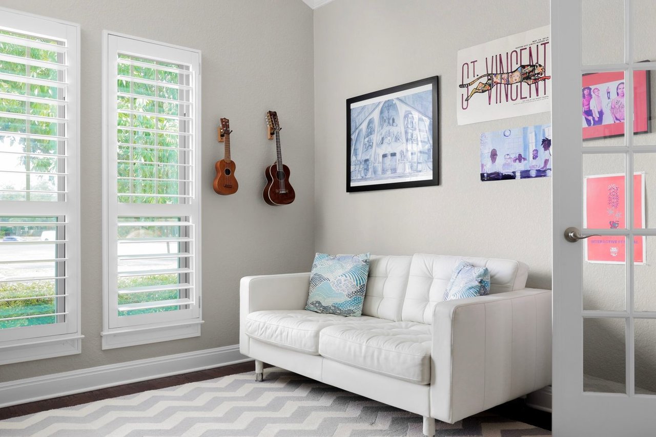 Living room with a white sofa, plantation shutters, wall-mounted ukuleles, and framed art.