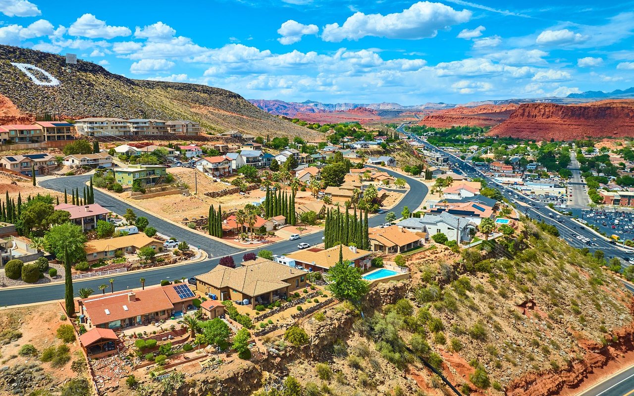 Hillside neighborhood of homes and winding roads beneath red-rock cliffs.