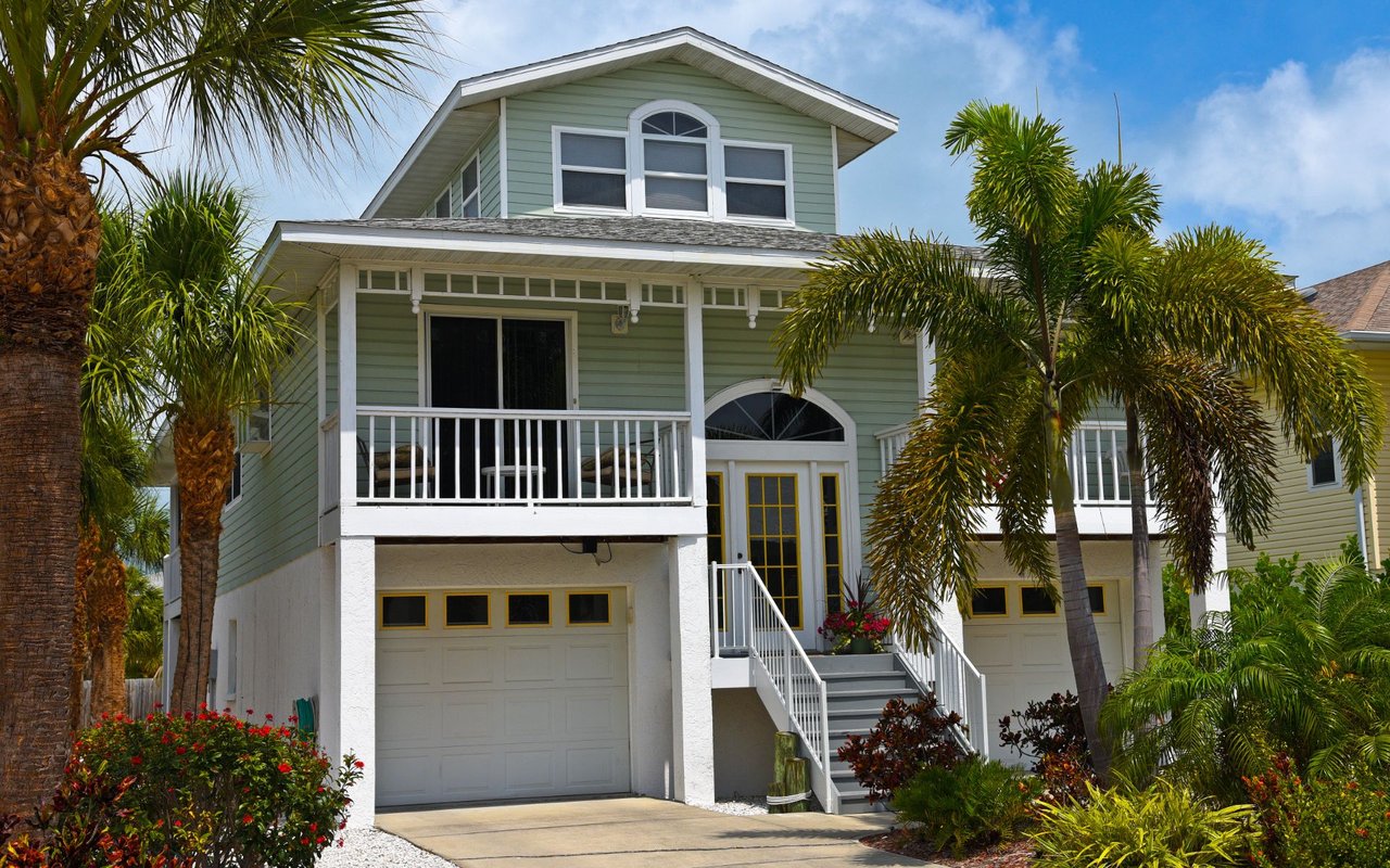 Pale green two-story home with a covered balcony, white trim, garage, and palm trees.