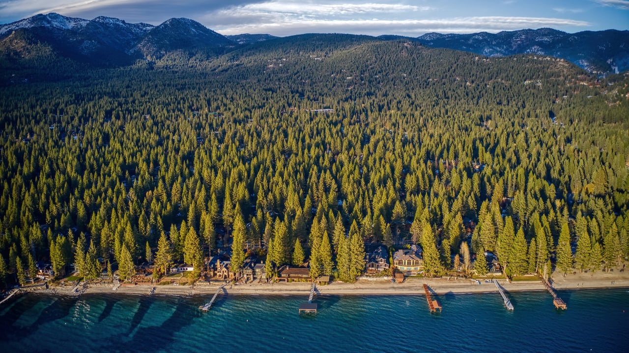 Aerial view of lakefront homes with private piers on Lake Tahoe in Incline Village, Nevada, with forest behind