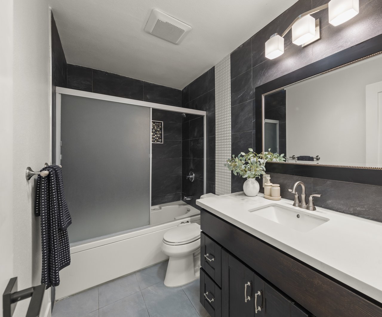 Bathroom with dark tile, a frosted sliding tub enclosure, and a dark vanity with a white countertop.