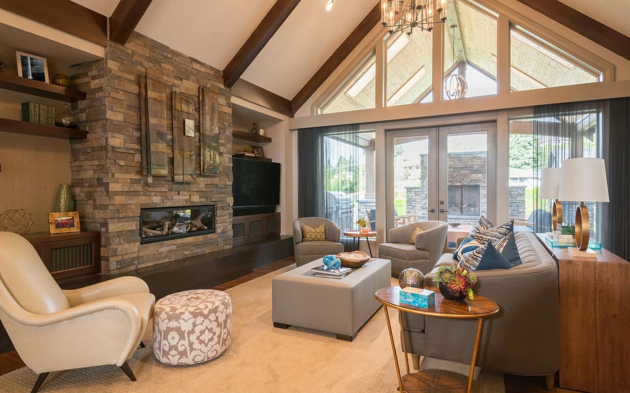 Vaulted living room with a stone fireplace, exposed beams, and expansive windows.