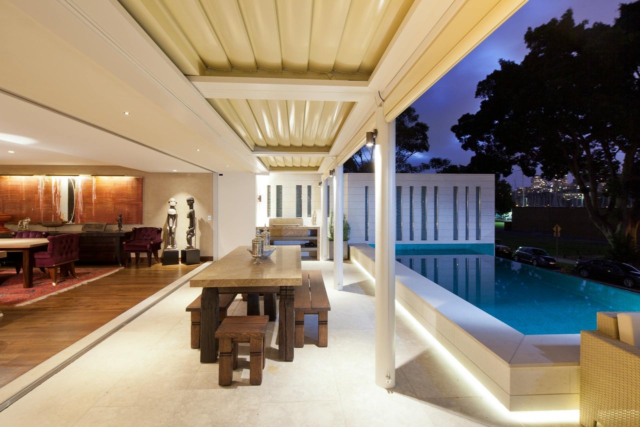 Luxury covered outdoor dining area with modern interior, poolside view, and ambient lighting at night