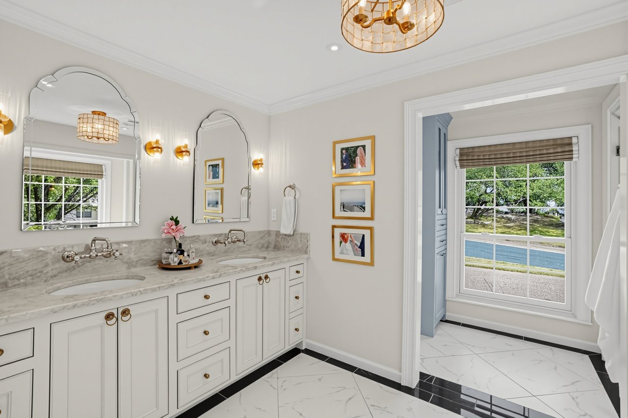 Bathroom with a double white vanity, marble counters, ornate mirrors, and brass fixtures.