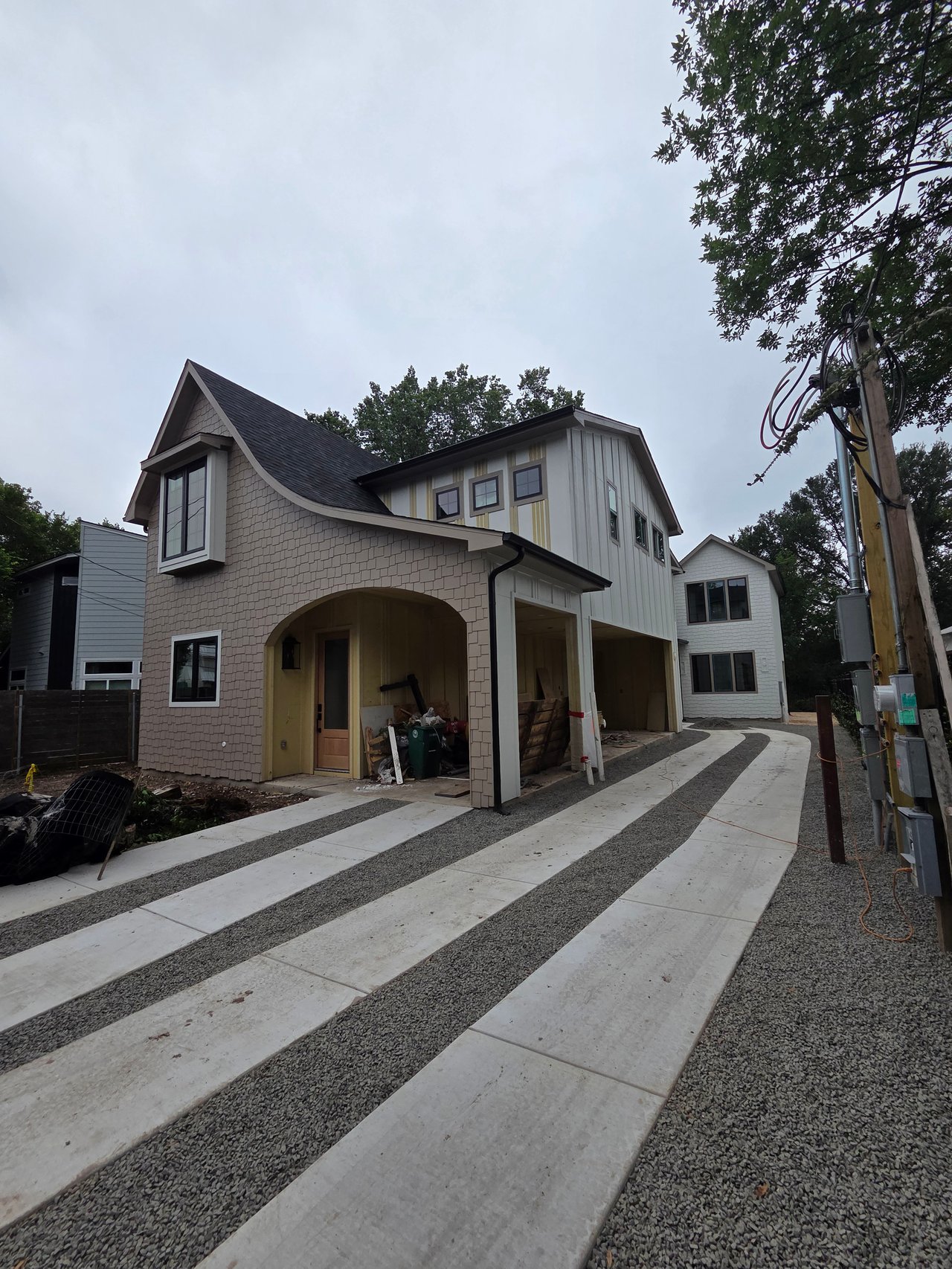House under construction with a steep gable roof and striped concrete-and-gravel driveway.