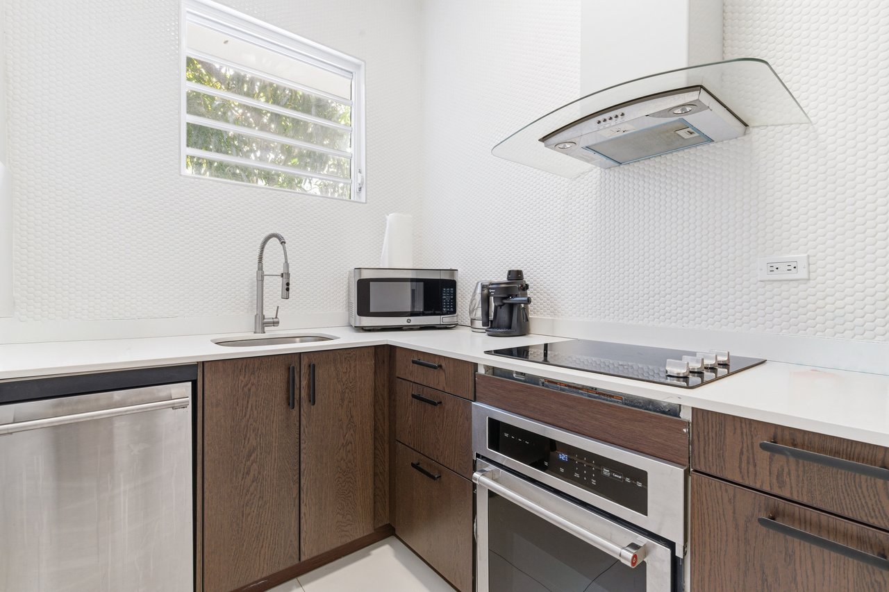 Compact kitchen with dark wood cabinets, a stainless-steel oven, and a white textured backsplash.