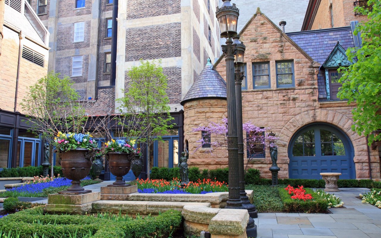 Landscaped courtyard with flower beds, ornate planters, and a tan stone building.