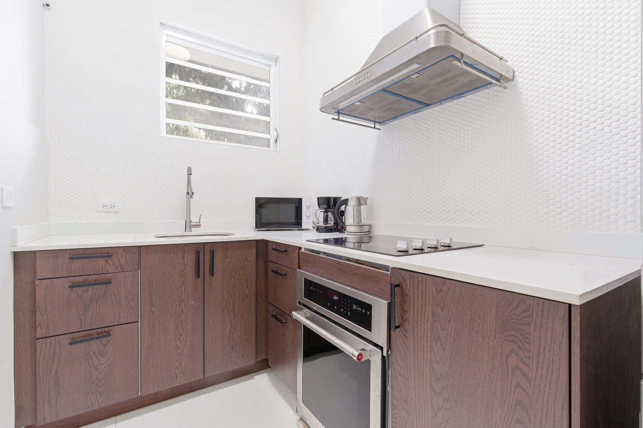 Modern kitchen with dark wood cabinets, white counters, and stainless-steel appliances.