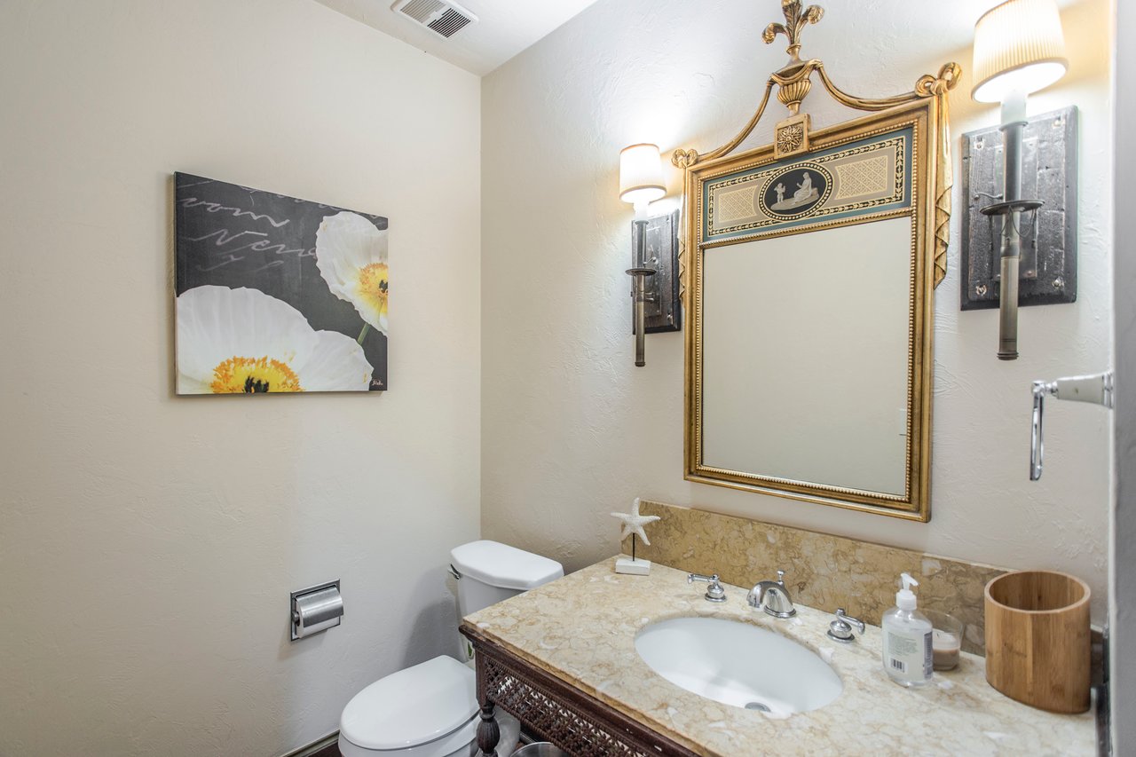 Bathroom with a marble vanity, oval sink, ornate gold mirror, and matching wall sconces.