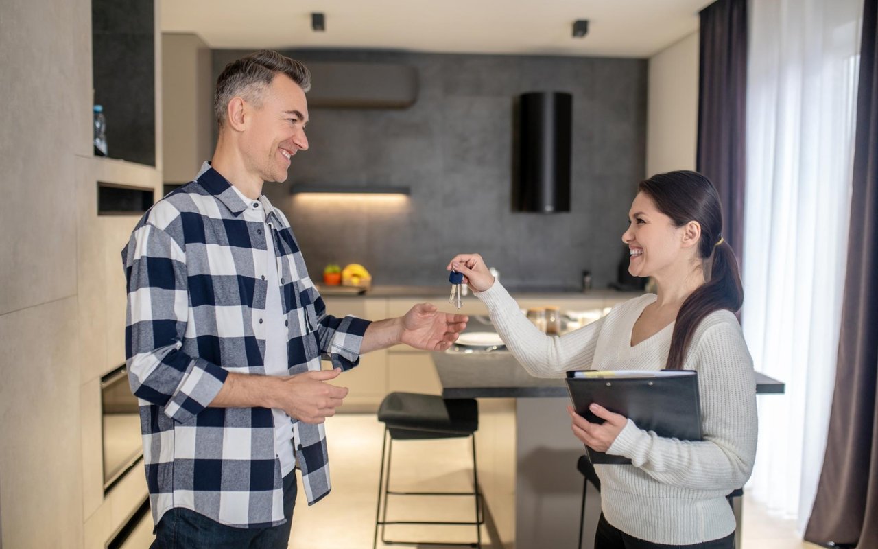A woman hands keys to a man in a modern kitchen.