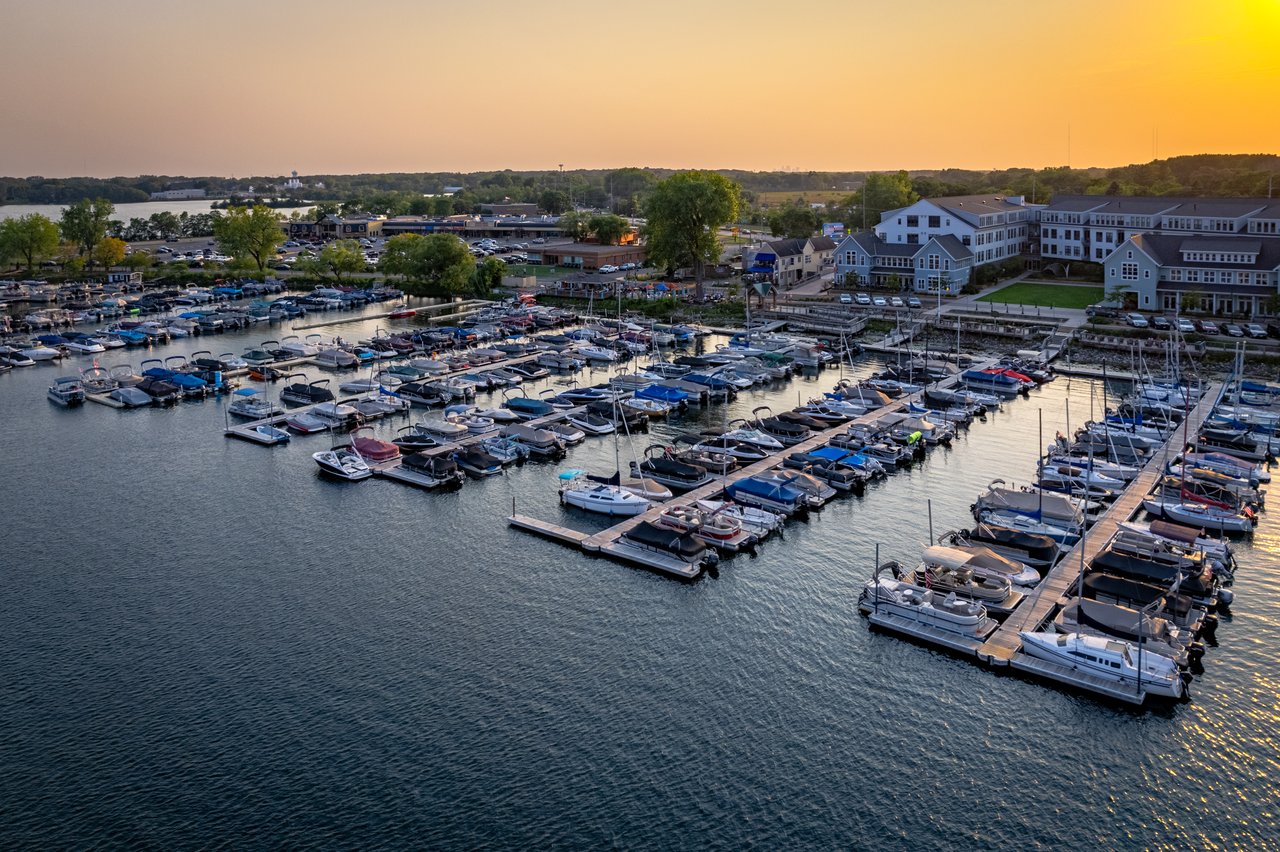 A marina crowded with boats and docks, with shoreline buildings beneath an orange sunset sky.